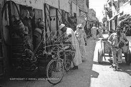 Image du Maroc Professionnelle de  Un homme accroche derrière sur son vélo une petite jarre pour retirer l'eau du puit dans rue situés derrière le cinéma Mabrouka où quelques artisans transformaient des pneus usagés en sceau pour hammam, cruche ou jarre que les paysans utilisaient pour faire sortir l’eau des puits. A cette époque le recyclage des pneus faisait partie intégrante du paysage social au Maroc, presque tous les hammams ont utilisés ces sceaux en caoutchouc à la place de ceux en bois, à cause de leur prix exorbitant et surtout qui se brisaient souvent par les lancements des ouvriers aux heures du nettoyage, Mercredi 18 Mai 1988. (Photo / Abdeljalil Bounhar) 